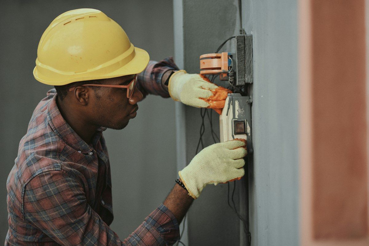 An electrician in a hard hat testing a switchboard