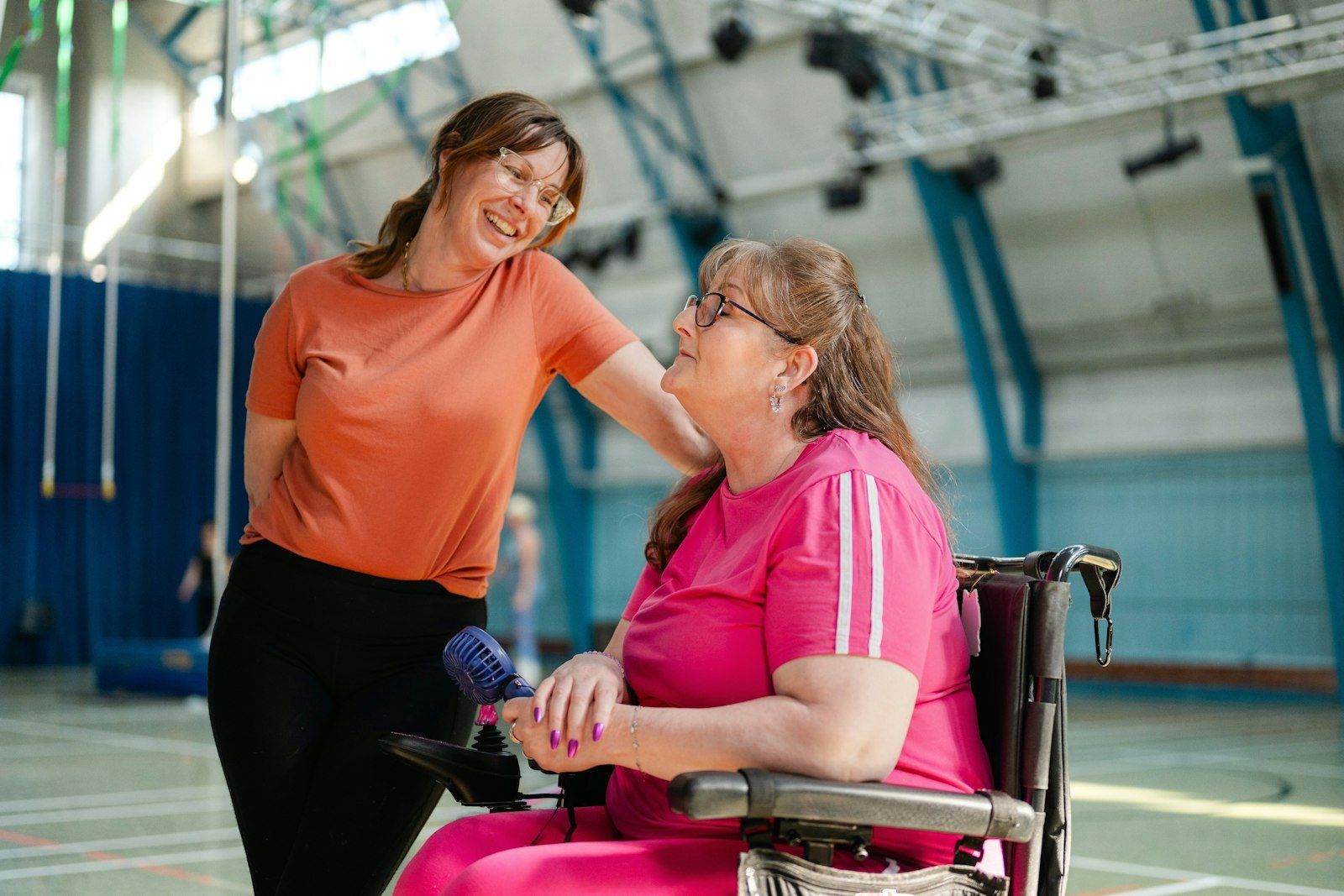 A support worker and a woman in a wheelchair laughing together in a gym